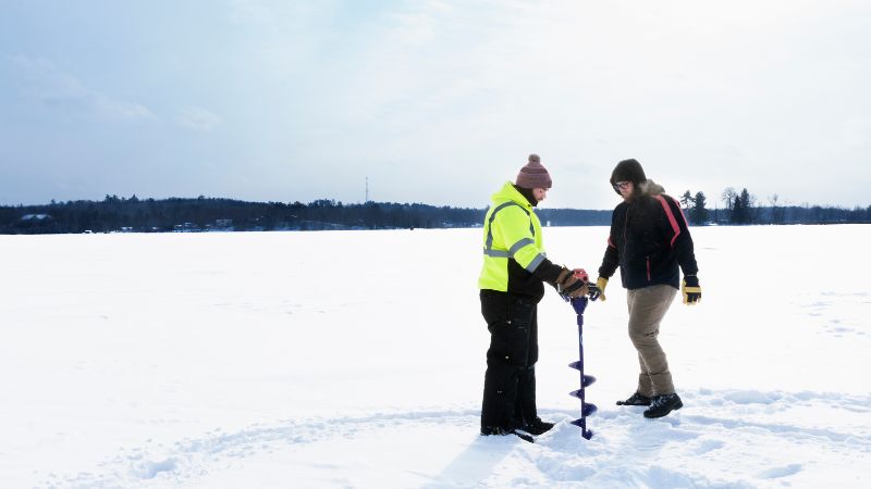 two people making a hole in the ice to go ice fishing