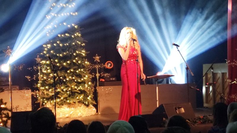 Alicia Blickfeldt singing on a stage with a Christmas tree in the background for an annual Christmas event