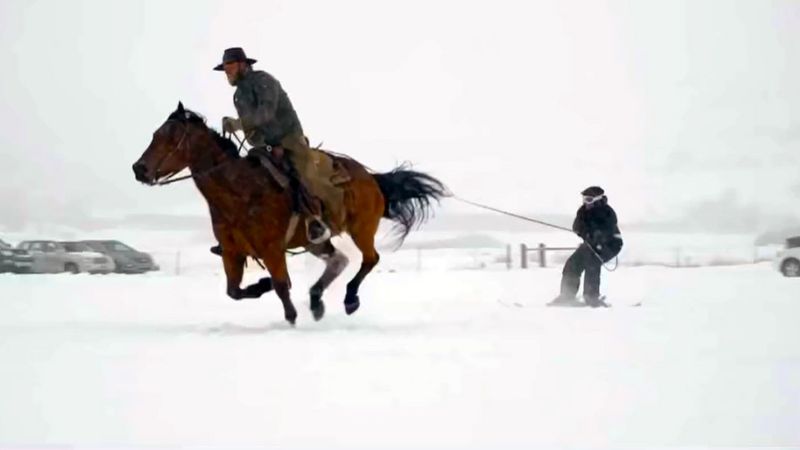 a man riding a horse with a man on skis being pulled behind the horse for the annual Skijoring event