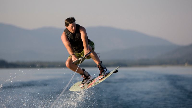 A wakeboarder in action, caught mid-air against a scenic backdrop of distant mountains and a calm lake.