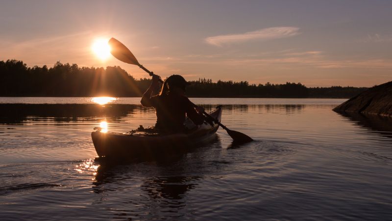 Person kayaking on a calm lake at sunset.