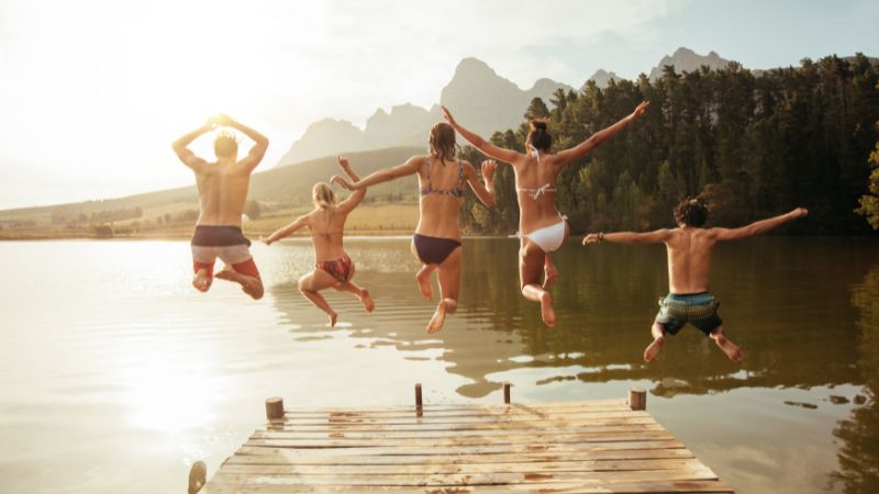Group of people jumping off a dock into a lake.